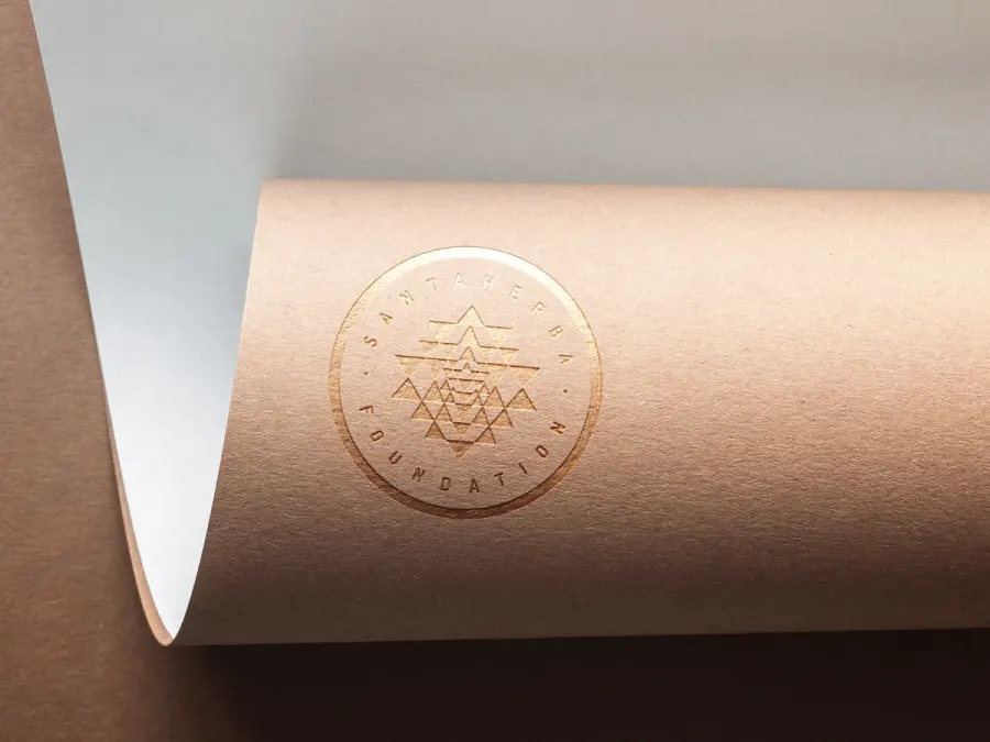 Okrągły znak Santa Herba Foundation wytłoczony złotą folią na zwiniętym arkuszu papieru kraft